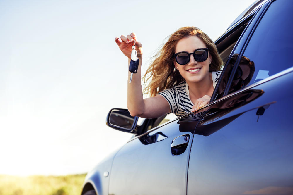 Happy woman leaning out of a car window and dangling car keys
